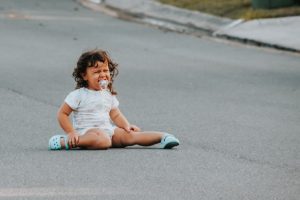 A toddler sits on the road in the W position crying